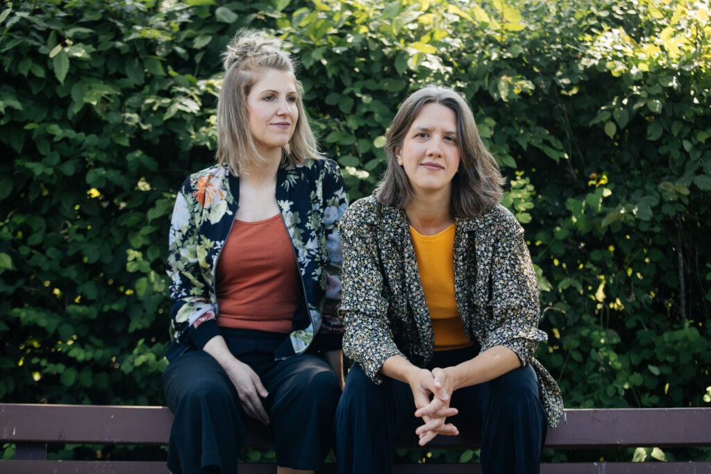 Wiebke Schröder und Sophia Grest sind das Duo Symarell. Sie sitzen auf einer Parkbank.